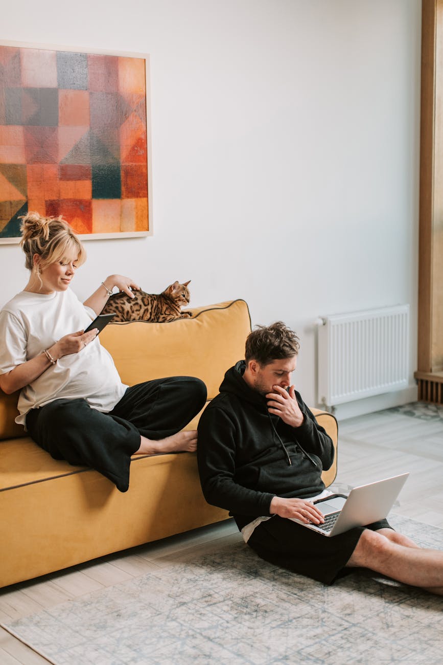 Pregnant woman and man relaxing on couch with Bengal cat in cozy living room environment. — Photo by Vlada Karpovich on Pexels