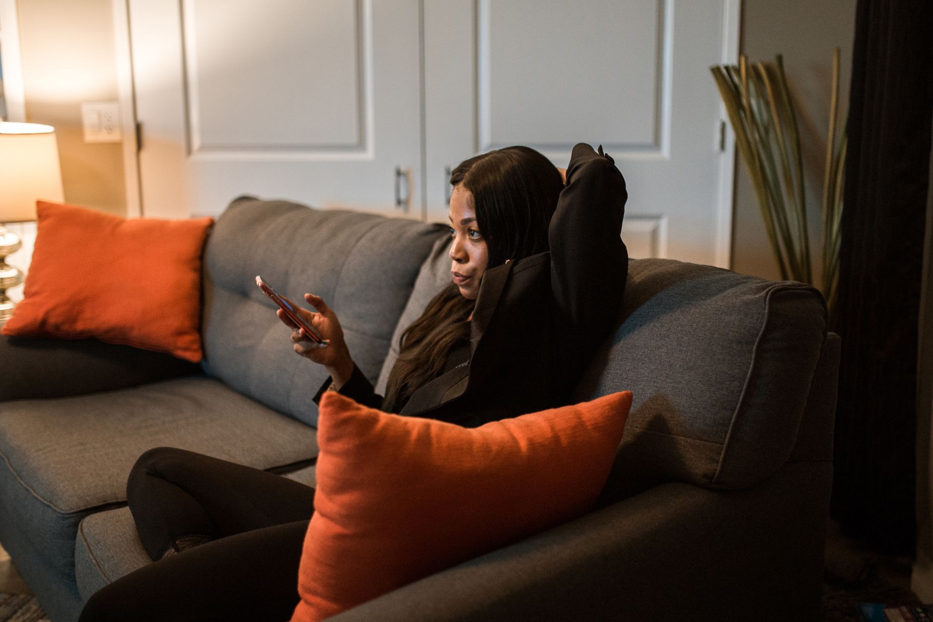 An African American woman in a black blazer relaxes on a sofa, engaging with her smartphone indoors. — Photo by RDNE Stock project on Pexels